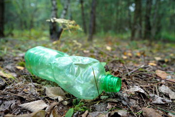Obraz premium Plastic bottle thrown away in forest. Garbage in nature, reusable products. Rubbish thrown in forest. PET Plastic water bottle thrown out in nature. Waste in nature. Abandoned pet garbage waste.