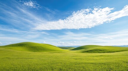 Obraz premium Rolling hills covered in green grass, beneath a clear blue sky with scattered white clouds. Peaceful and natural.