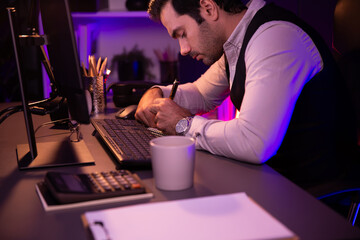 Smart businessman writing memo market data on paper work report folder to analyze sales channel online of discipline's product service at purple neon dark light room at late night time. Surmise.
