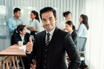 Portrait of happy businessman looking at camera, make approval hand gesture thumb up with motion blur background of business people movement in dynamic business meeting. Habiliment