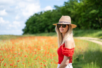 Young blonde woman in sunglasses and straw hat on a field of red poppies