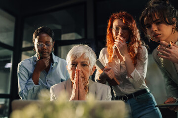 Serious boss looking at the laptop at office with her interracial team