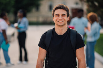 Portrait of male student standing at campus and smiling at camera.