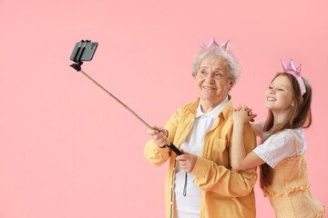 Little girl with her grandmother in crowns taking selfie on pink background
