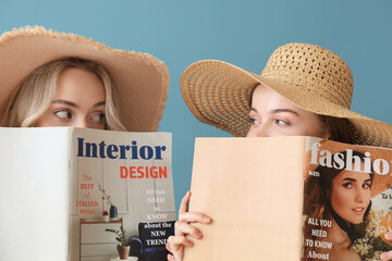 Young sisters in summer hats reading magazines on blue background, closeup