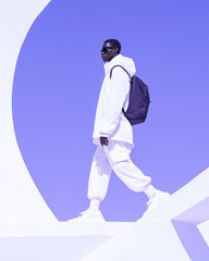 A young man in white pants and a jacket walks against a bright blue sky.