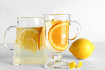 Glass cup and jug of infused water with lemon on light background