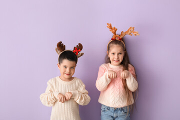 Cute little children in deer horns and knitted sweaters on lilac background