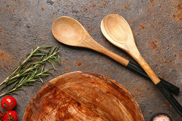 Wooden kitchen board, spoons, rosemary and tomatoes on grunge background
