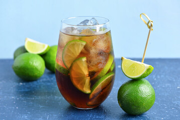 Glass of cold Cuba Libre cocktail and limes on blue table