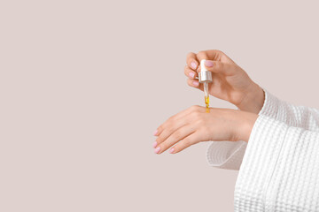 Hands of woman with cosmetic oil on light background