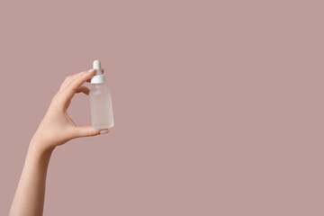 Hand of woman with bottle of cosmetic oil on pink background