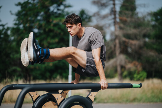 Young man performing abdominal exercise on parallel bars in a park. Outdoor fitness and health-focused activity.