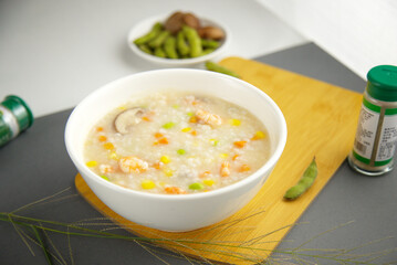 Close-up of porridge of shrimp and shiitake mushrooms in a white bowl, edamames