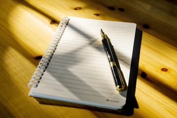Close-up notebook and pen on wooden table with sun shining, light and shadow