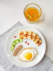 Close-up of fried egg, ham sausage, bread and cucumber on white plate, top view