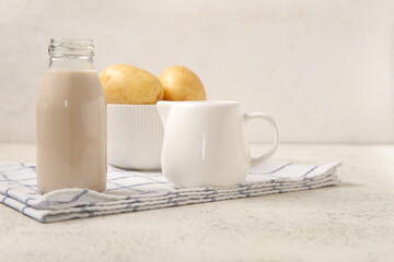 Bottle and jug of tasty potato milk on light background