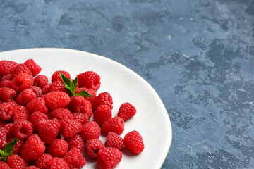 Plate with fresh raspberries and mint on blue background