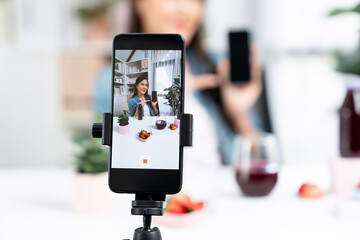 Selective focus smartphone with smiling young beautiful Asian reviewing mixed strawberry and cherry juice detox drink, presenting healthy product promotion selling on social media online. Stratagem.