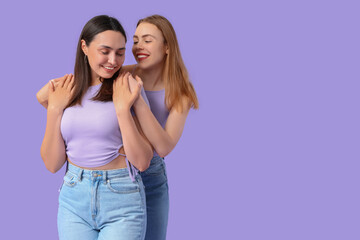 Fototapeta premium Beautiful young lesbian couple on lilac background