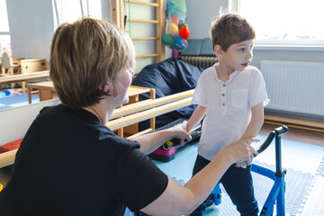 Male child with cerebral palsy actively participates in physical therapy with his therapist in a rehabilitation center during a training session with walker