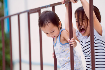 Obraz premium Cute boy playing climbing iron fences in the playground in summer with sisters, bright smiles of children, the love of sibling playing together happily. Excitement and fun come with a wide imagination