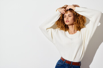 Fashion portrait of a woman wearing a cozy white sweater, posing casually against a light...