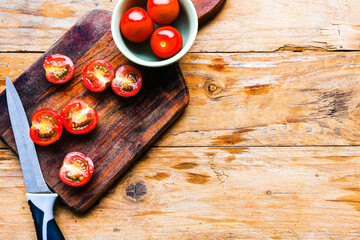 A wooden cutting board with a knife on it and a bowl of tomatoes