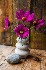 A vase with purple flowers sits on a wooden table beside a rock. The flowers are arranged in a way that they are all facing the same direction, creating a sense of harmony and balance