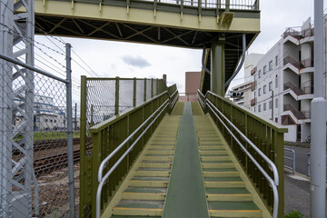 A pedestrian bridge with a bike ramp for wheeling bicycles up leads over a railroad track above a Japanese residential street. Nagoya, Japan