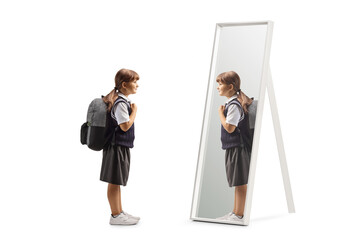 Girl in a school uniform standing with a backpack on shoulders and looking at a mirror