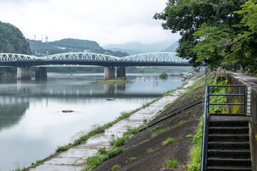 Obraz premium Peaceful and serene riverbank scenery of Kiso River in Japan with Inuyama Bridge over the water in the background. 犬山橋