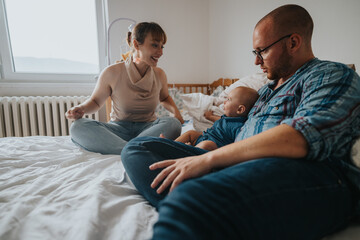 A joyful family spending quality time in a cozy bedroom, featuring parents engaging lovingly with their baby. The warm, intimate scene captures the essence of family connection and happiness.