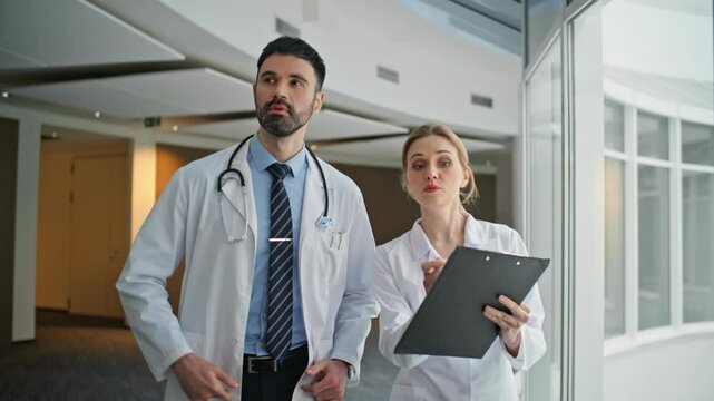 Physicians discussing health treatment pointing clipboard. Two doctors walking