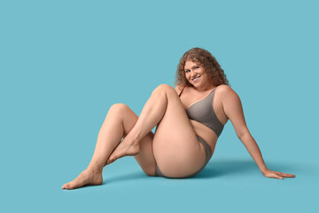 Beautiful young happy body positive woman in stylish underwear sitting on blue background