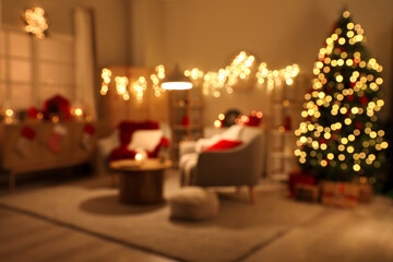 Blurred view of living room with armchairs, Christmas tree and glowing lights at night