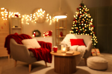 Blurred view of living room with armchairs, Christmas tree and glowing lights at night