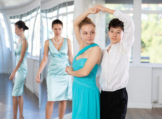 Couple of teenagers in festive clothes learn to dance latin american dance Bachata in studio under...