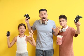 Father and his children with popcorn playing video game on yellow background