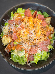 High angle view of Cesar salad with chicken and bacon in a dark bowl