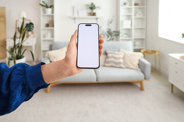 Woman with blank mobile phone in living room, closeup
