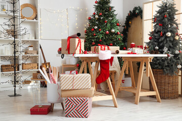 Beautiful gift boxes with packing materials and decorations on table near Christmas trees at home