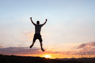 Silhouette of a man jumping with arms raised in celebration against a stunning sunset backdrop. The image conveys the concept of celebrating life and motivation for success