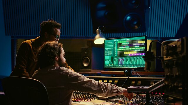 Musician and producer work on soundboard pads at professional studio station. Sound designer uses digital mixer in music production, operating on sliders and key buttons at control desk. Camera B.