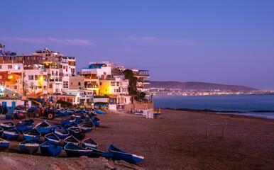 Taghazout, small fishing and surfing village with sandy beach, boats and traditional Moroccan buildings near Agadir, Morocco at sunset. Popular seaside resort among surfers.