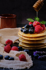 pancakes with berries and honey on dark background