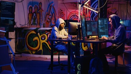 Team of hackers typing fast on keyboards in graffiti painted hideout, rushing to finish developing...