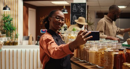 Zero waste store employee filming their natural products in recyclable jars, working on online commercial. Woman records video presenting homemade ethically sourced items on sale. Camera 2.