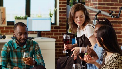 Diverse group of people throwing birthday party for their friend, drinking alcoholic beverages and eating gourmet cheese. Smiling guests laughing in cozy living room after gifting host presents