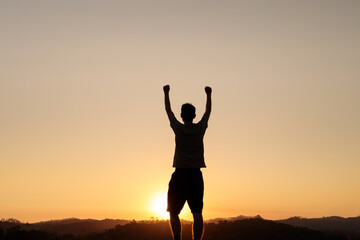 Fototapeta premium With arms raised in victory, a person stands silhouetted at sunset. This image captures a moment of achievement, success, and personal triumph in nature